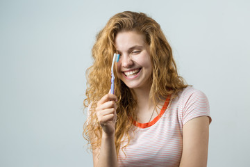 Portrait of a smiling cute woman with red curly hair holding toothbrush isolated on a white background