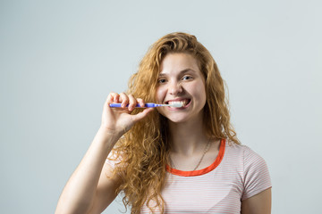 Portrait of a smiling cute woman with red curly hair holding toothbrush isolated on a white background