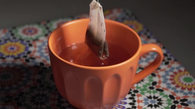 Italy - June 23, 2019: Slow motion tea bag dipped in hot water contained in an orange cup to prepare a hot drink.