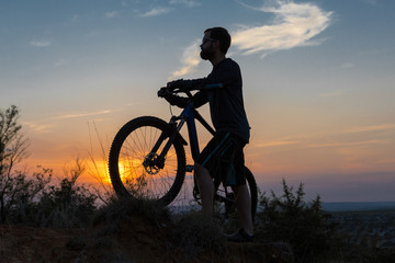 Obraz premium Cyclist in shorts and jersey on a modern carbon hardtail bike with an air suspension fork rides off-road on the orange-red hills at sunset evening in summer 