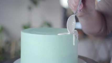 confectioner makes exquisite drips of white glaze over turquoise surface of cake