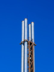 Four metal pipes against a blue sky. Ecological problems.