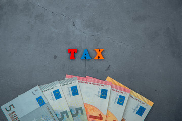 The multicolored tax word is made of wooden letters on a grey plastered wall background.