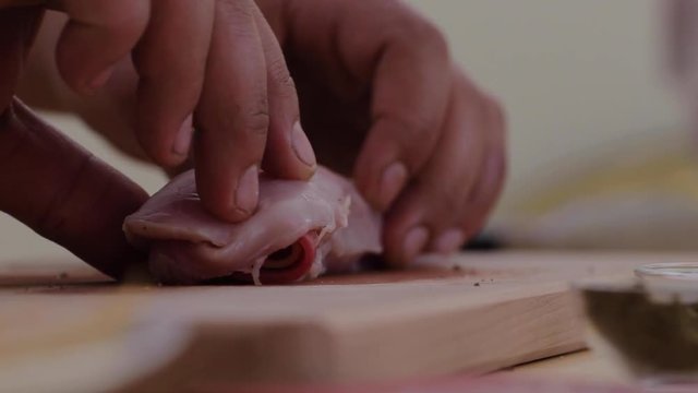 Hands measuring the size of a piece of stuffed Chicken breast cordon blu on a wooden chopping board