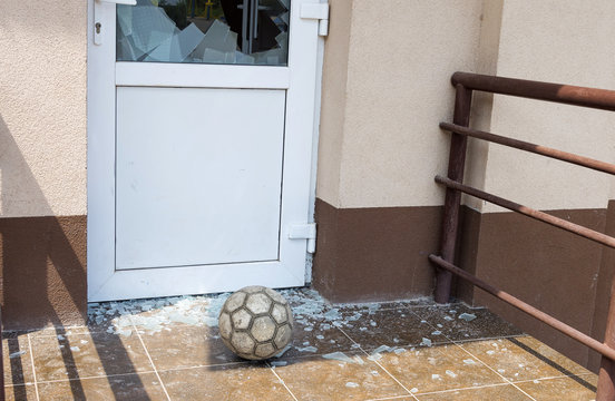A soccer ball broke the window. Football and broken window glass. Close-up, selective focus.
