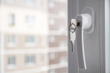 Handle with lock and key on the PVC window. Apartment house on the background. Closeup, selective...