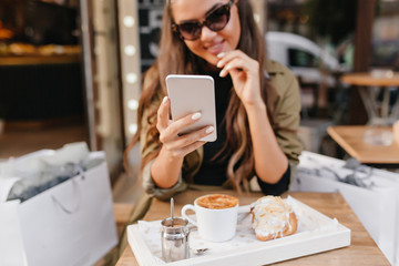 Portrait of tanned lady with elegant manicure and cup of latte on foreground. Smiling brunette...