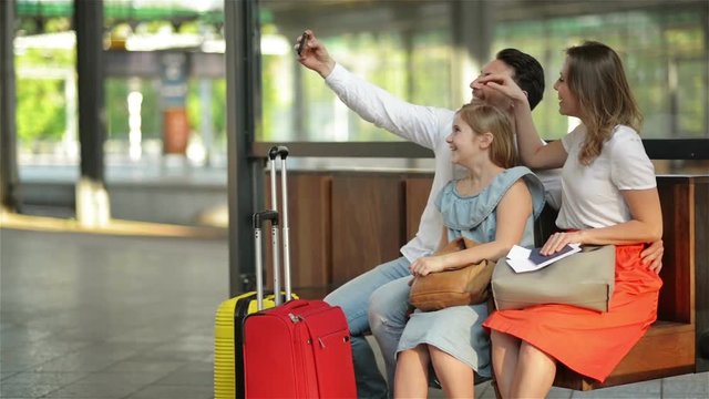 Vacation Time Rocks. Smiling Beautiful Family Taking Selfie With Smartphone While Waiting For Their Flight At Airport or Train At Railway Station.