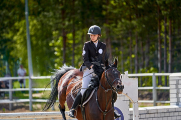 A young woman jockey on a horse performs a jump across the barrier. Competitions in equestrian sport. Close-up.
