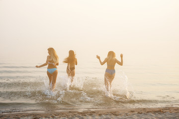 Three beautiful young women running to the sea.