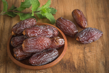 close up picture of dates palm fruit in cup and mint on wooden table background. Dates palm fruit dry is snack healthy.