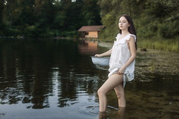 Young laundress stands in a river and holds a basin in her hands.