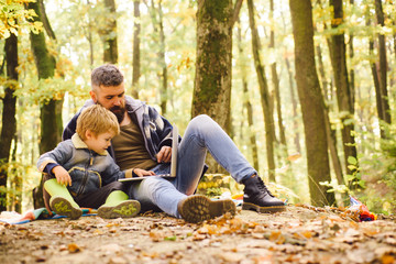 Naklejka na ściany i meble Modern family. Ecology lesson. Forest school and ecology education. Man bearded father and son with laptop in forest. Ecology upbringing. Father teaches son use modern technology. United with nature