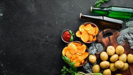 A bottle of beer and Potato chips with spices on a black background. Snacks to beer. Top view. Free space for text.