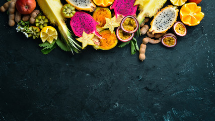 Tropical fruits - passion fruit, pineapple, dragon fruit, kiwi and cactus on a black background. Top view. Free space for text.
