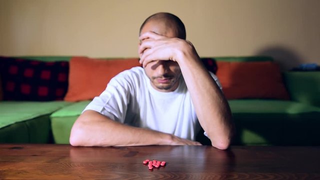 Depressed man suffering from suicidal depression want to commit suicide by taking strong medicament drugs and pills pain killers while he sitting in his dark room selective focus moody dramatic look