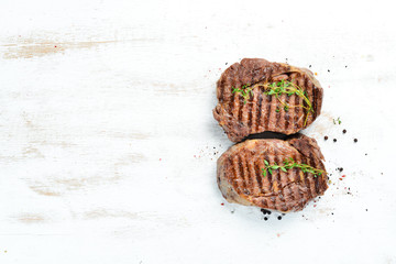 Grilled ribeye beef steak, herbs and spices on a white wooden background. Top view. Free space for...