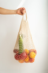Female hand holding cotton string bag with fresh fruits and vegetables