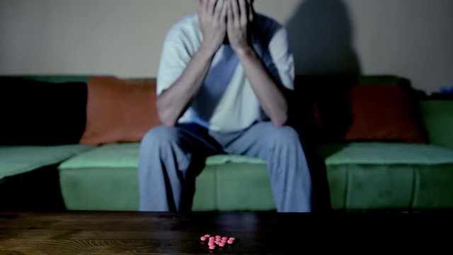 Depressed man suffering from suicidal depression want to commit suicide by taking strong medicament drugs and pills pain killers while he sitting in his dark room selective focus moody dramatic look