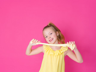 beautiful 10 year old girl is playing with yellow slime in front of pink background and is happy