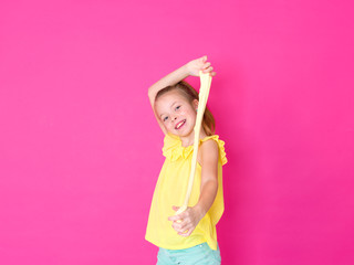 beautiful 10 year old girl is playing with yellow slime in front of pink background and is happy