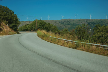 Road passing through hilly landscape with wind turbines