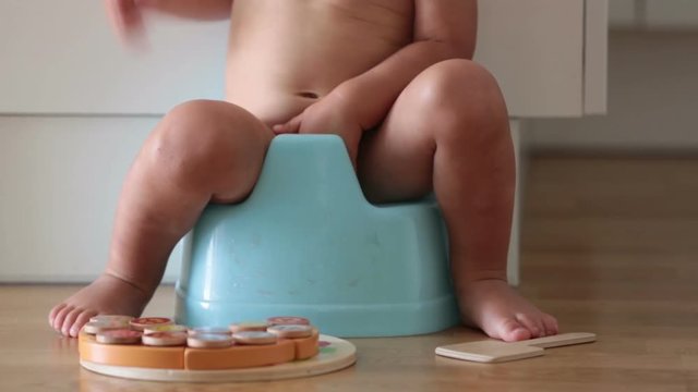 Little toddler boy, sitting on potty, playing with wooden toy at home