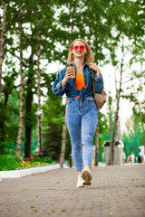 Fototapeta premium Young Blonde Girl in blue jeans walking in summer park