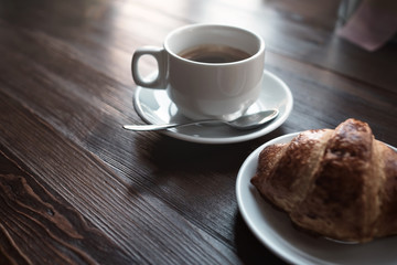 Cup of coffee and croissants on wooden table background.