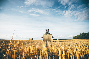 Couple with dog having fun with hay stack on wheat field on warm summer evening.