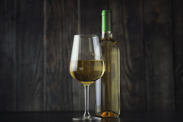 Transparent bottle of white dry wine on the table. White wine glass on a wooden background.