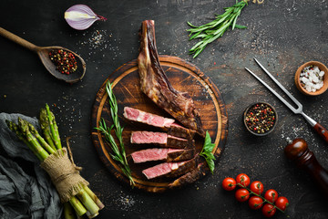 Grilled steak on the bone, herbs and spices on a wooden background. Barbecue. Top view. Free space...