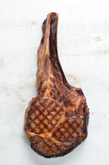 Grilled steak on a bone on a white wooden background. Barbecue. Top view. Free space for text.