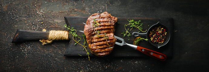 Fototapeta Grilled ribeye beef steak, herbs and spices on a dark table. Top view. Free space for your text. obraz