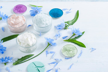 moisturizers, bath salts and powder compacts with blue chicory flowers on white wood table