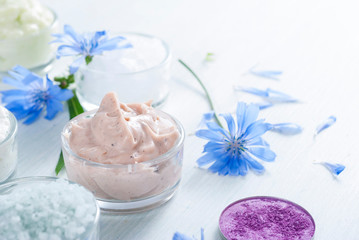 moisturizers, bath salts and powder compacts with blue chicory flowers on white wood table