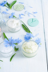 Obraz na płótnie Canvas moisturizers, bath salts and powder compacts with blue chicory flowers on white wood table