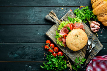 Burger with Prosciutto on old wooden background. Breakfast. Top view Free space for your text.