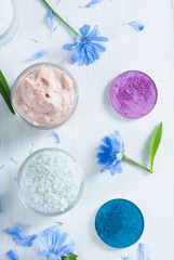 moisturizers, bath salts and powder compacts with blue chicory flowers on white wood table
