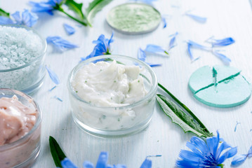 moisturizers, bath salts and powder compacts with blue chicory flowers on white wood table