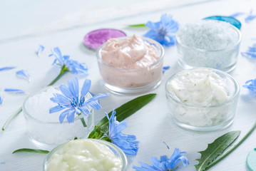 Obraz na płótnie Canvas moisturizers, bath salts and powder compacts with blue chicory flowers on white wood table