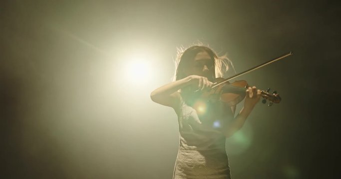 Professional female violin player performing an amazing solo during concert, spotted by light on smoked black background 4k footage