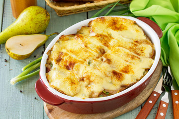 Potato gratin with pear, raclette cheese, and bacon on rustic wooden table. Traditional french cuisine.