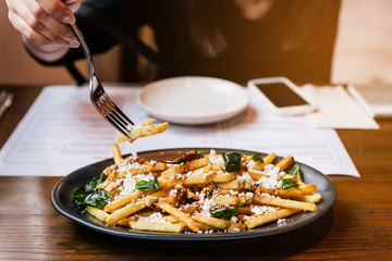 Hand pinching French fries with fried basil, Thai chili and feta cheese with fork. Thai fusion food.