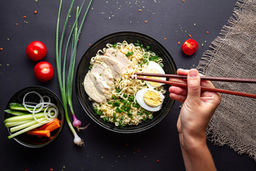 Ramen noodles black bowl with chicken, vegetables, chives and egg on black background Top view.