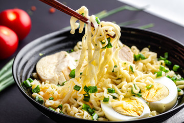 Ramen noodles close up with chicken, vegetables and egg on black background