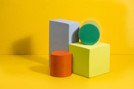 Geometric shapes in different colors on yellow background. Three-dimensional solid figures on colored paper.