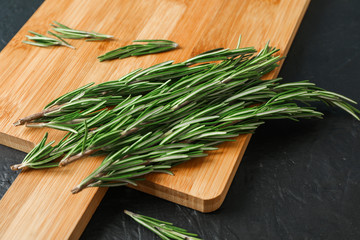 Cutting board with green rosemary on black background, space for text