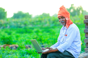 Young indian farmer with laptop at field