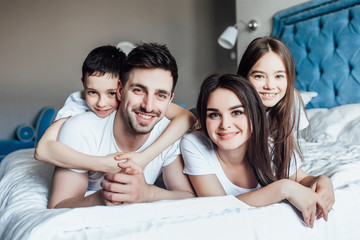 Happy smiling young family with kids lying in bed, portrait in bedroom.
